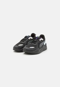 Ein Paar schwarze Sportschuhe aus Mesh- und Synthetikmaterialien, mit weißen Streifen und schillernden Akzenten, auf einem weißen Hintergrund gezeigt.