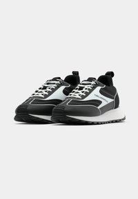 Crne i sive atletske tenisice s bijelim vezicama, elegantnog dizajna, gornjište od teksturirane mreže i kontrastni naglašeni panel sa strane.