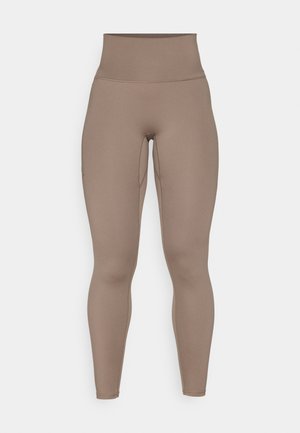 Høyt liv, tettsittende leggings i en glatt, matt, lys brun stoff med sidesømmer og uten synlige logoer eller mønstre.
