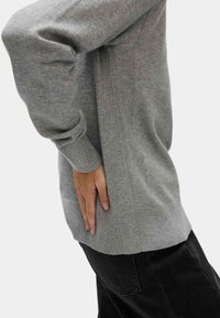 Szary, dzianinowy sweter z prążkowanymi mankietami i szwami bocznymi, w połączeniu z czarnymi spodniami. Tekstura wydaje się miękka i lekko luźna.