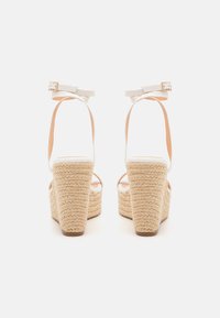 Sandales blanches à talons compensés avec une plateforme en corde de jute. Présentent des sangles au niveau des chevilles et une semelle texturée. Vue arrière mettant en avant le design empilé.