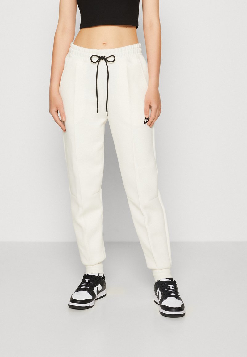 Joggers blancs et effilés avec cordon de serrage noir, poches latérales et un petit logo Nike noir sur la cuisse gauche. Associés à des baskets noir et blanc.