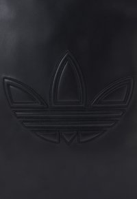 Black leather product featuring embossed three-leaf logo design with horizontal stripes. Smooth texture with a matte finish.