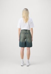 Denim šorti ar gaismas un tumši zila gradientu, augsta josta, četriem kabatām un nedaudz nodilušu tekstūru.