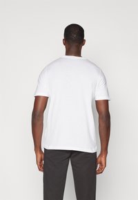 Witte T-shirt met korte mouwen, gemaakt van katoen, met een ronde hals en een relaxte pasvorm, gecombineerd met donkere broeken. Eenvoudig en minimalistisch ontwerp.