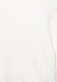 Biała polarowa bluzka o miękkiej, teksturowanej powierzchni. Charakteryzuje się prostym fasonem i luźnym krojem. Brak widocznych elementów metalowych i wzorów.