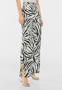 Kalhoty s širokýma nohavicema v černobílé zebra vzoru, s bočními rozparky a hladkým, lehkým materiálem. Navrženy s vysokým pasem.