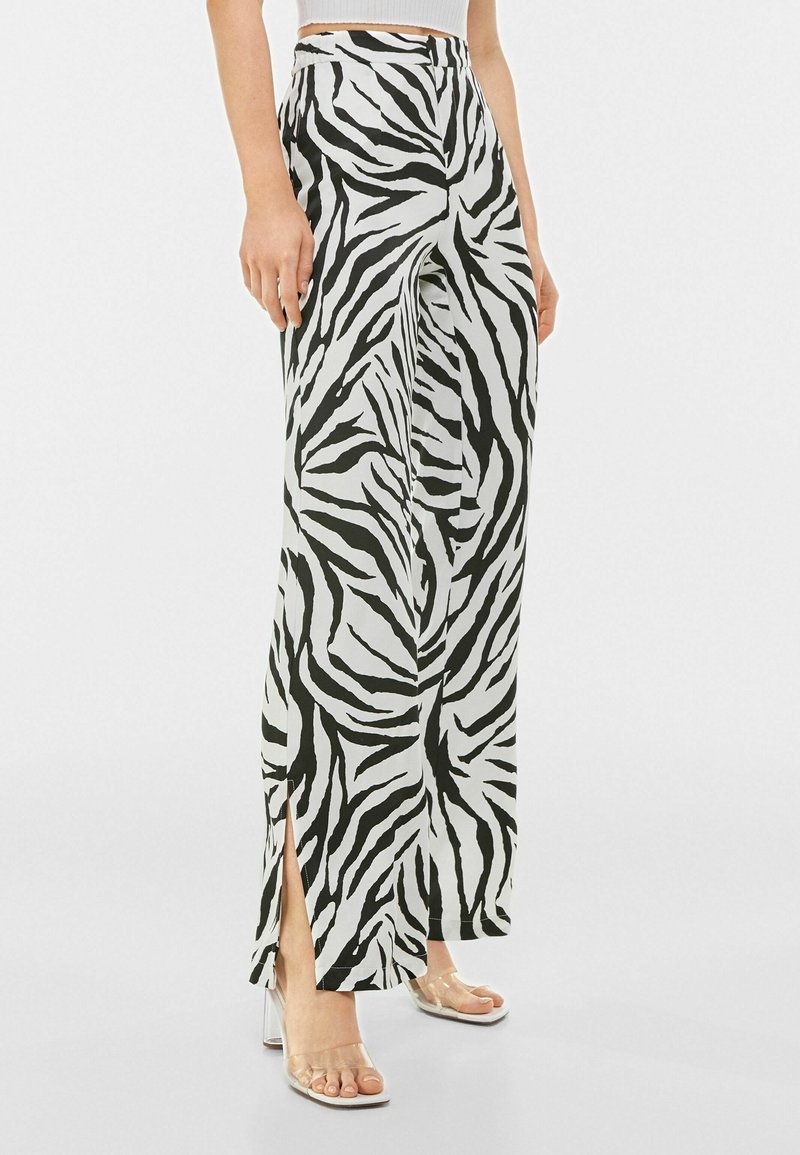 Kalhoty s širokýma nohavicema v černobílé zebra vzoru, s bočními rozparky a hladkým, lehkým materiálem. Navrženy s vysokým pasem.