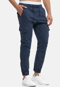 Pantalones de carga azul marino con puños elastizados, cintura con cordón, bolsillos frontales y bolsillos laterales con parche. Fabricados con un tejido duradero y de textura suave.
