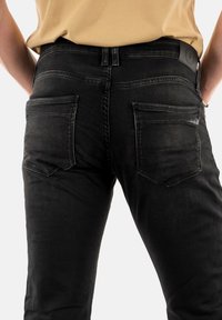 Jeans in denim nero con una vestibilità slim. Le caratteristiche includono tasche posteriori con design a patta e una patch in pelle testurizzata sulla vita.