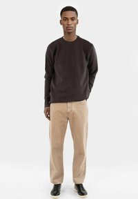 Mörkbrun crewneck sweatshirt, beiga corduroybyxor, svarta sneakers. Slät tygkvalitet, avslappnad passform, lång ärm och raka ben.