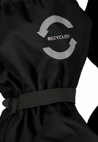 Giacca nera realizzata in materiale riciclato, con un tessuto testurizzato, vita elastica e un logo di riciclaggio stampato in grigio.