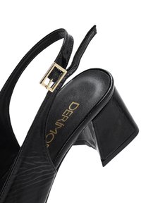 Black patent leather slingback shoe with a square toe, chunky heel, and gold buckle detail on the strap. Textured upper with logo.