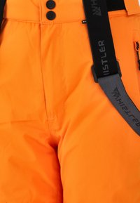 Orange snöbyxor med svarta justerbara remmar, med två svarta knappar och en liten dragkedjeficka på sidan, med en slät yta.