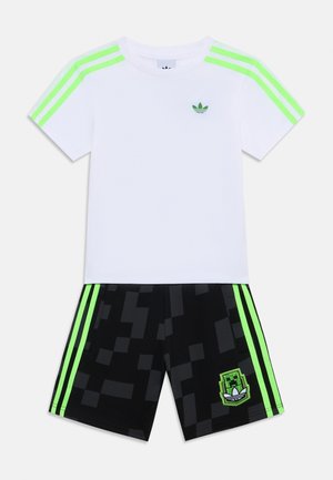 T-shirt branca com detalhes verdes e três riscas nas mangas, combinada com calções pretos com um padrão pixelado e um logo verde.