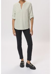 Light green, striped collared shirt with roll-up sleeves paired with black slim-fit trousers and black loafers featuring gold hardware.