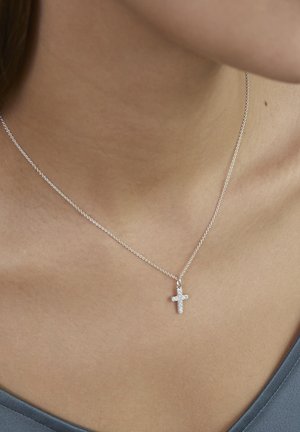 Delicate zilveren ketting met een klein kruisvormig hangertje, versierd met kleine steentjes, gedragen om de nek en het sleutelbeen van een persoon.