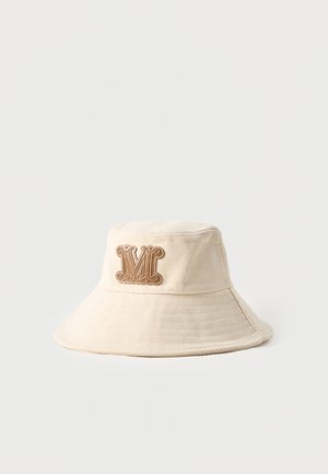 Béžový látkový klobúk typu bucket s širokou krempou a vystúpenou hnedou nášivkou s písmenom "M" vpredu v strede.