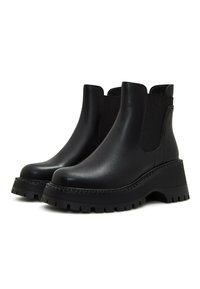 Bottes noires en cuir à hauteur de cheville avec semelles crantées épaisses, panneaux latéraux élastiques et languette à l'arrière pour un enfilage facile.