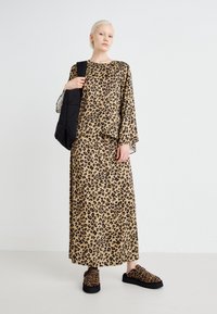 Outfit a stampa leopardata composto da una maglietta ampia con maniche larghe e una gonna lunga coordinata. Borsa nera imbottita e ciabatte a stampa leopardata.