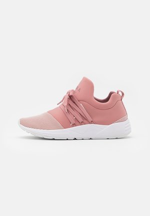 Różowy niski sneaker z siateczkowym noskiem, grubą białą podeszwą, szerokimi sznurowadłami związanymi w kokardę oraz pętelką na pięcie, pokazany z profilu na białym tle.