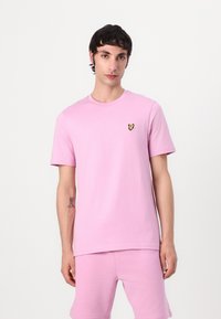 Rosa kortärmad t-shirt i bomull, med rund halsringning och en liten gul fjärilslogga på vänster bröst.