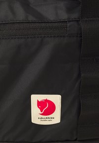 Black fabric bag featuring a horizontal zip pocket, with a cream-colored label displaying a red fox logo and "FJÄLLRÄVEN Sweden 1960."