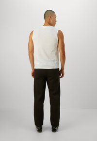 Hvid ærmeløs top med en tekstureret overflade, parret med løstsiddende sorte bukser. Bagfra ses et enkelt design og en afrundet kant.