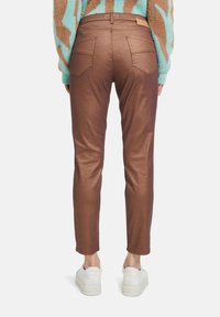 Braun metallische Skinny-Jeans mit zwei Gesäßtaschen, hoher Taille und glattem Textur, kombiniert mit weißen Sneakers.