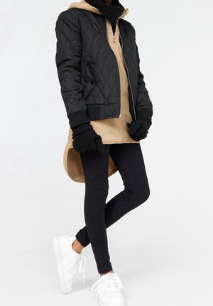 Quiltet sort bomberjakke, beige hættetrøje med lynlås under, sorte leggings og hvide sneakers. Sorte handsker fuldender looket.