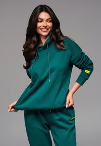 Felpa verde acqua con cappuccio, cordoncini e tasche laterali. Caratterizzata da polsini a coste e un piccolo logo giallo cucito sulla manica.