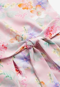 Tela con estampado floral en rosa pastel que presenta varias flores en púrpura, naranja y blanco, con un detalle de lazo atado en la cintura.