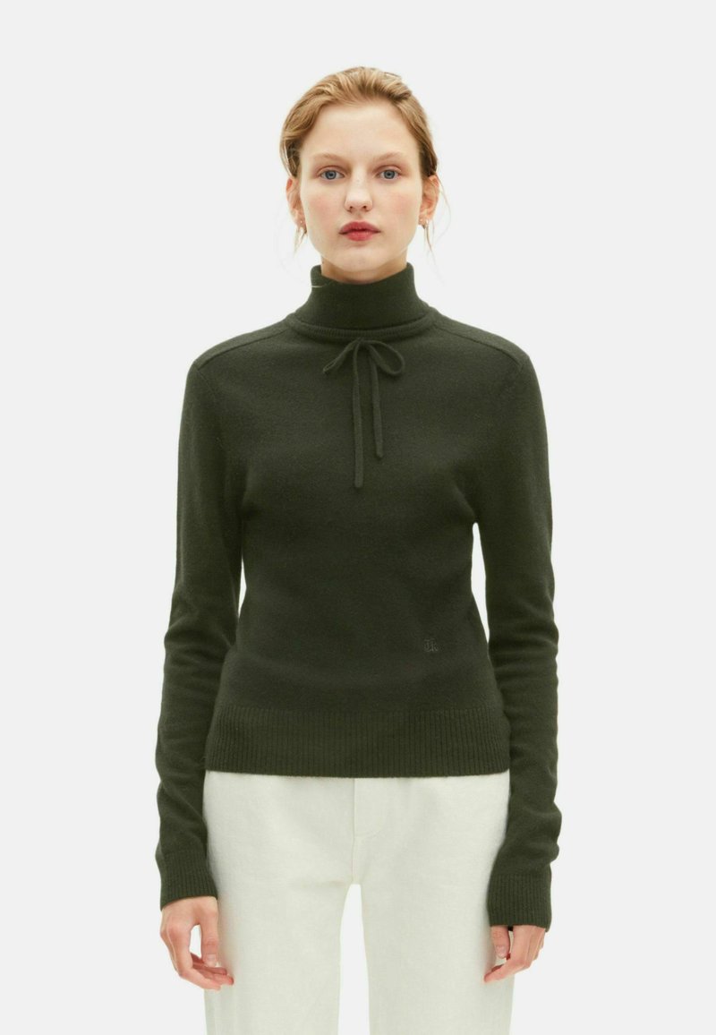 Suéter de cuello alto verde oscuro con un detalle de lazo en la parte delantera, puños y dobladillo acanalados, hecho de material suave, diseño ajustado.