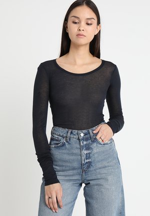 Black long-sleeve top in sheer fabric with a rounded neckline, paired with high-waisted light blue denim jeans featuring a classic fit.