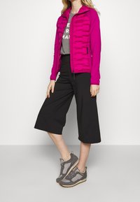 Fuchsia puffer jacket with a hood, quilted texture, two side pockets, worn over a gray T-shirt and paired with black culotte pants and gray sneakers.