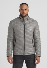 Graue Steppjacke mit strukturiertem Material, hohem Kragen, Reißverschluss vorne und seitlichen Taschen. Verfügt über kontrastierende schwarze Reißverschlüsse.