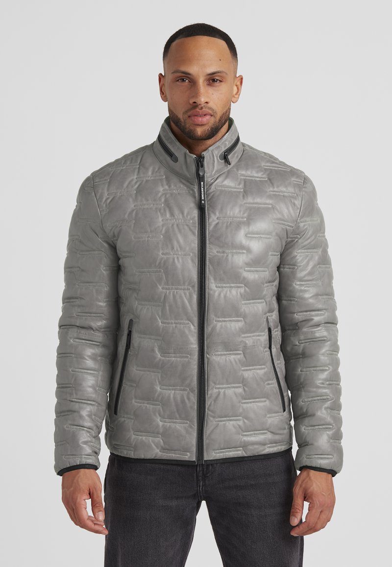 Graue Steppjacke mit strukturiertem Material, hohem Kragen, Reißverschluss vorne und seitlichen Taschen. Verfügt über kontrastierende schwarze Reißverschlüsse.