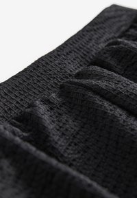Tissu noir texturé avec un motif froissé. Le matériau a une apparence légère et tissée avec des variations subtiles dans le motif.
