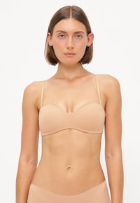 Nude-colored strapless bra with a smooth texture and molded cups; minimalistic design, narrow shoulder straps, and seamless finish.
