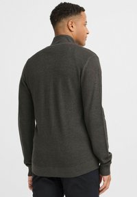 Pull en tricot gris foncé avec un col montant, un motif texturé, des poignets et un ourlet côtelés. La vue de dos montre une silhouette légèrement ajustée.