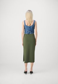 Denim avkortet topp med justerbar bakside, kombinert med skjørt i lang olivengrønn farge med sidesplitt, komplettert med svarte hæl-mules.