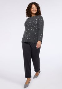 Grijze trui met zilveren pailletten, lange mouwen, gecombineerd met zwarte taps toelopende broek en grijze puntige hakken. Soepele textuur, ontspannen pasvorm, modern ontwerp.