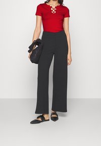 Top rojo ajustado con escote cruzado, combinado con pantalones de pierna ancha negros de cintura alta. Los accesorios incluyen un bolso negro trenzado y zapatos planos negros.