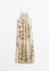 Robe nuisette crème avec fines bretelles et grands imprimés de feuilles tropicales marron suspendue sur fond blanc.