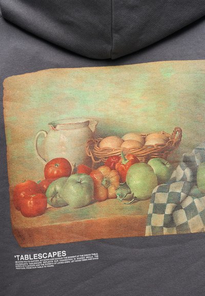 Natiurmortas su keraminiu ąsočiu, krepšeliu kiaušinių, pomidorais, obuoliais, paprikomis ir languotu audiniu ant medinio stalo.