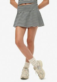 Gambe incrociate con una gonna a righe bianche e nere, calzini color crema e sneakers beige New Balance.