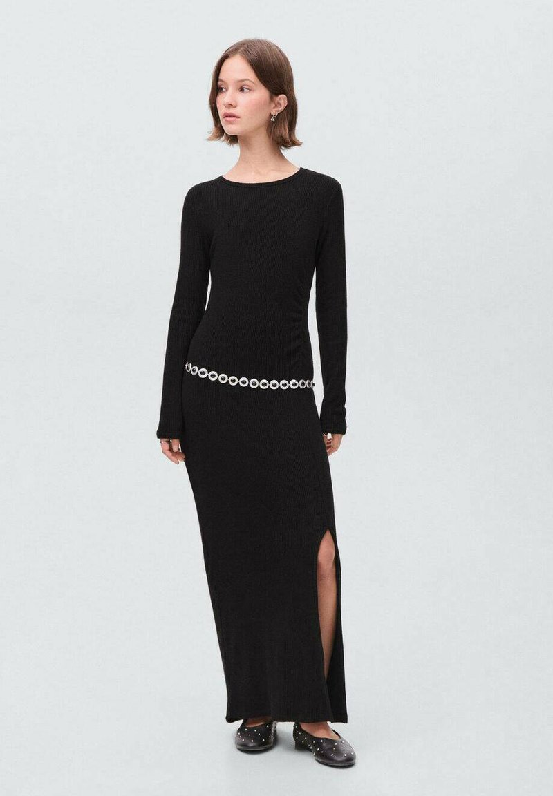 Robe maxi noire côtelée avec des longues manches, une fente sur le côté et une ceinture avec un détail circulaire. Texture lisse et design ajusté.