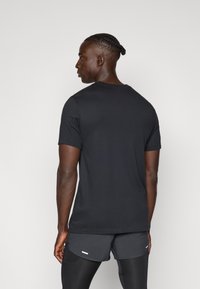 Μαύρο βαμβακερό μπλουζάκι με κλασικό λαιμόκοψη, κοντά μανίκια και λεία υφή, προσανατολισμένο από την πλάτη, συνδυασμένο με σκοτεινές βερμούδες.