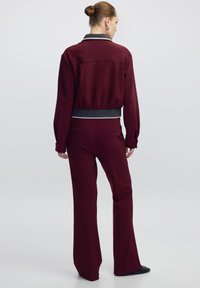 Bordeaux trainingspak met een korte, ritsjack met een geribbelde kraag en bijpassende wijde broek met een gladde textuur en strak ontwerp.