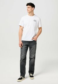 Valkoinen puuvillainen crew neck -t-paita, jossa on painettu teksti rinnassa, yhdistettynä tummanharmaisiin suoriin farkkuihin ja mustavalkoisiin tennareihin.
